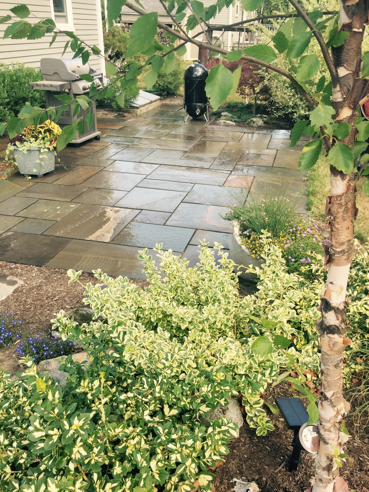 stone patio with grilling station alongside garden